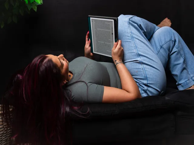 Victoria Rojas stretched out on a couch reading from a backlit e-reader, knees drawn up